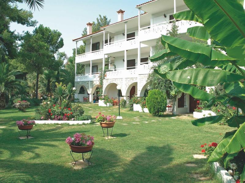 Großes dreistöckiges Haus mit weißen Wänden, Balkon und üppigem grünem Garten mit Pflanzen und Büschen.