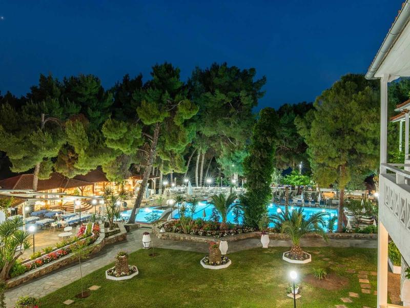 Nachtansicht eines beleuchteten Schwimmbads mit umliegenden Gebäuden und Bäumen.