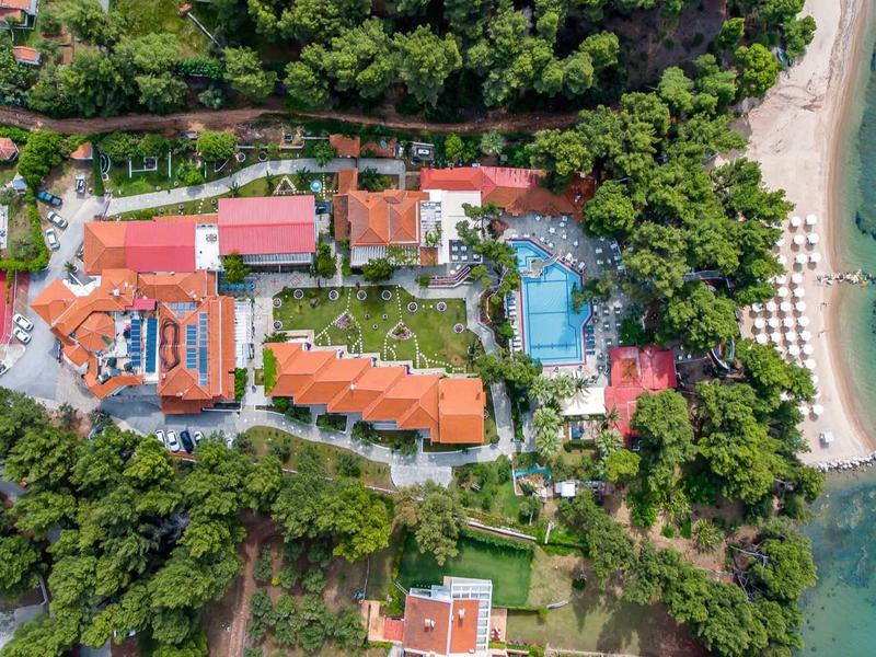 Vogelperspektive auf Hotel mit Pool, Tennisplatz, Grünflächen und Strand an türkisblauem Meer.