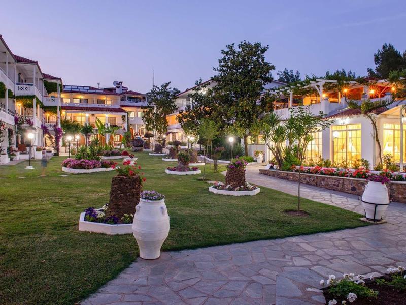 Ein gepflegter Garten mit Wegen, Statuen und beleuchteten Gebäuden im Abendlicht.