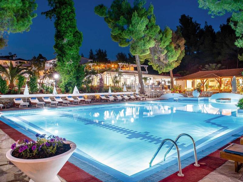 Beleuchteter Swimmingpool mit Poolliegen, Blumen und Bäumen in einer ruhigen Abendumgebung.