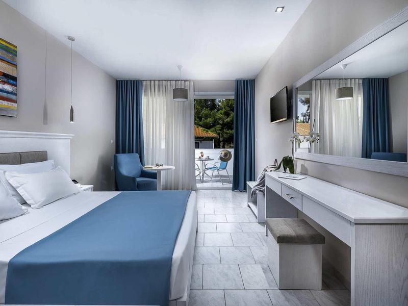 Modernes Schlafzimmer mit weiß-blauem Farbschema, großem Fenster, TV und Schreibtisch mit Spiegel.