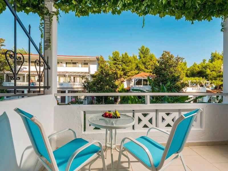 Balkon mit blaugrünen Stühlen, kleinem Glastisch und Aussicht auf grüne Bäume und Häuser.