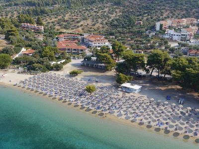 Pobřežní pláž s organizovanými řadami slunečníků a lehátek poblíž zelených kopců.