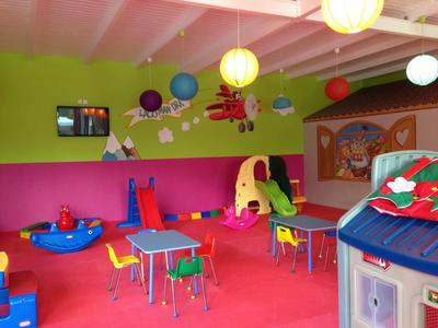 Barevná dětská herna s malými stoly, židlemi, hračkami a světlými nástěnnými dekoracemi.