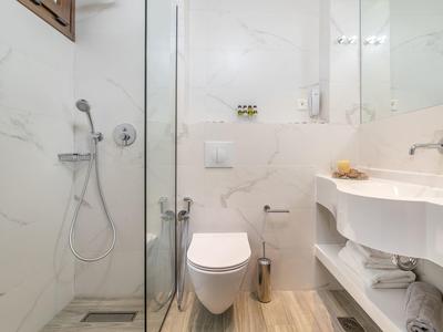 Moderní hotelová koupelna s walk-in sprchou, závěsným WC a bílou umyvadlovou skříňkou.