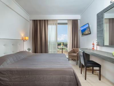 Moderní hotelový pokoj s manželskou postelí, pracovním stolem, židlí a velkým oknem s výhledem na město.