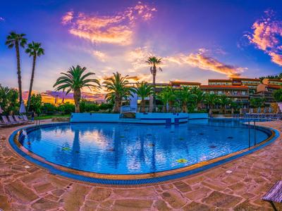 Runder Pool mit Palmen und Hotelgebäude bei Sonnenuntergang.