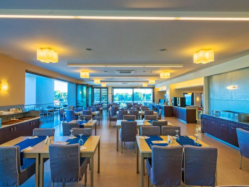 Moderní hotelová restaurace s modrými židlemi a prostřenými stoly.