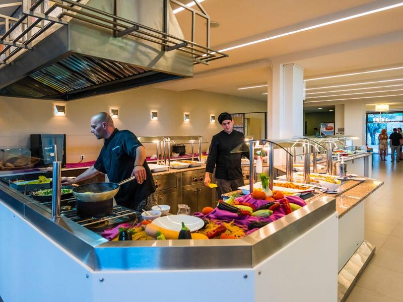 Rušná hotelová kuchyně s kuchaři připravujícími čerstvá jídla na velkém moderním pultu.