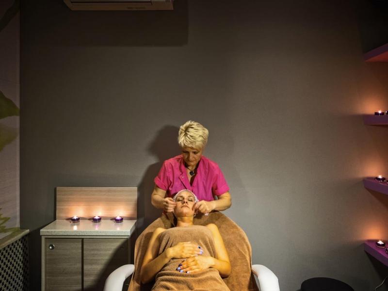 Osoba dostává uvolňující masáž hlavy v tlumené spa místnosti se svíčkami a měkkým osvětlením.