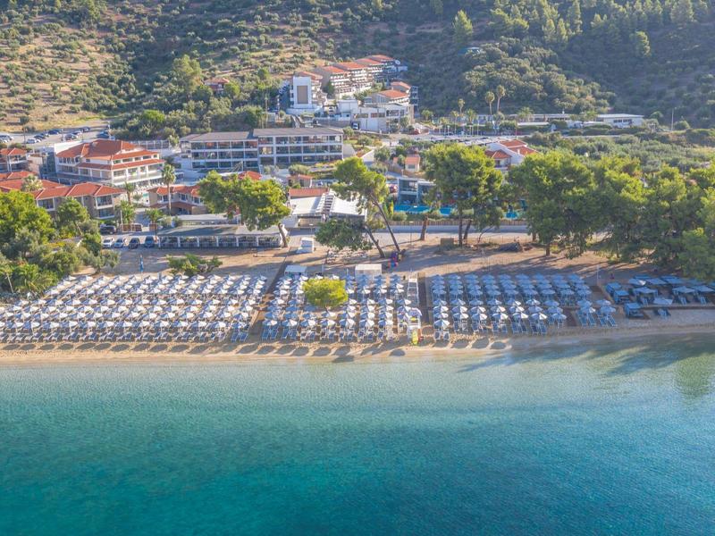 Large plage de sable avec parasols devant un hôtel et des collines boisées