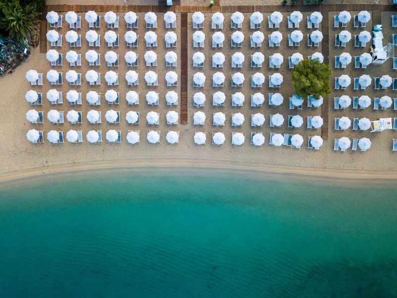 Vue aérienne d'une plage avec des parasols blancs disposés symétriquement et de l'eau turquoise.