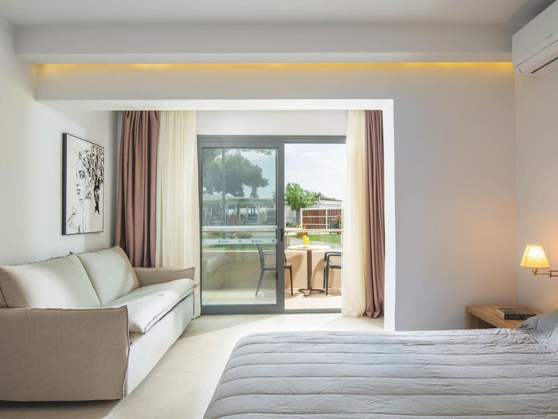 Chambre d'hôtel moderne avec lit double, canapé et accès à une terrasse avec vue.