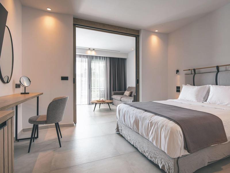 Chambre d'hôtel moderne avec lit double, bureau et salon mitoyen.