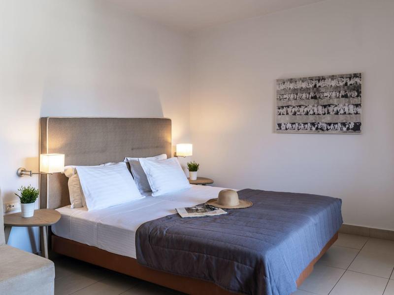 Chambre d'hôtel lumineuse avec lit double, literie grise, deux tables de nuit et décoration minimale.