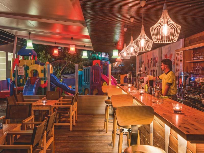 Bar intérieure avec comptoir en bois et coin salon à côté d'une aire de jeux pour enfants intérieure.