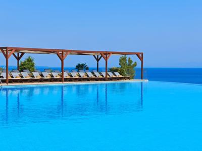 Unendlicher Pool mit Liegestühlen und Pergola mit Blick auf das Meer bei klarem Himmel.