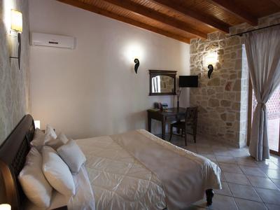 Helles Schlafzimmer mit Holzbalken, Steinwand, großem Bett, Schreibtisch und Glas-Tür zum Garten.