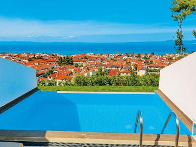 Blaue Poolanlage mit Blick auf rote Dächer, grünes Feld und blauen Himmel am Meer.