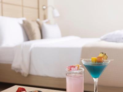 Ein Holztablett mit frischem Obst, rosa Getränk und blauem Cocktail vor einem Bett.