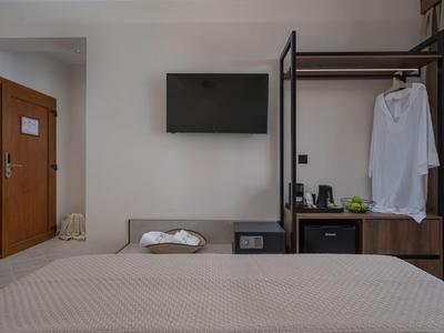 Ein schlicht eingerichtetes Hotelzimmer mit Bett, Wand-TV und offener Garderobe mit Bademantel.