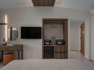 Moderner Hotelzimmer mit Bett, Wandfernseher, Schminktisch, Spiegel und offener Kleiderschrank.