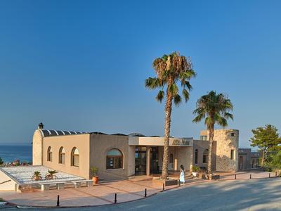 Modern beige hotel building with palm trees under clear blue sky by the roadside.