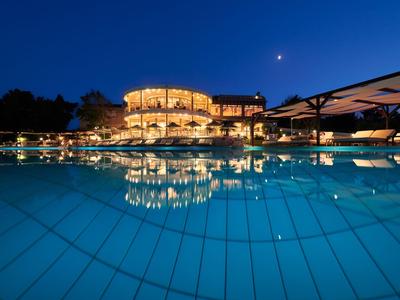 Illuminated hotel building at dusk with pool and clear water, moon in night sky.