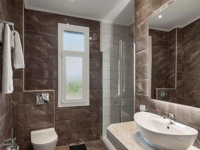 Modern bathroom with brown tiles, toilet, round sink, and large mirror.