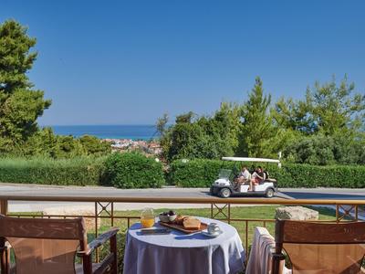 View of a set table on a terrace overlooking a golf cart and the sea.