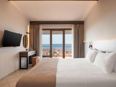 Modern hotel room with double bed and sea view through panoramic windows.