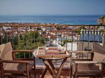 Balcony with table and two chairs overlooking a green valley and the sea.
