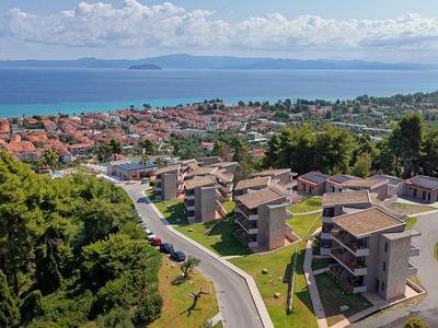 View of a coastal town with buildings, greenery, and a winding road by the sea.