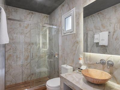 Bright bathroom with wood flooring, marble walls, glass shower, and modern fixtures.
