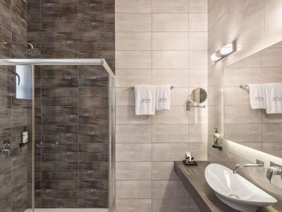 Modern hotel bathroom with walk-in shower, light tiles, and wooden ceiling beams.