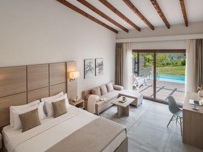 Modern hotel room with double bed, seating area, and view of pool and garden.