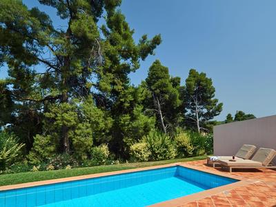 A clear pool next to a terrace with two lounge chairs in front of a wooded backdrop.