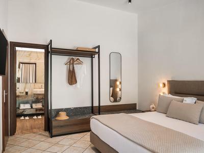 Modern hotel room with double bed, open wardrobe, and entrance to the bathroom.