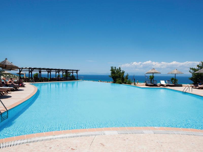 Großer Infinity-Pool mit blauer Wasseroberfläche, Liegestühlen und klarem Himmel am Meer.
