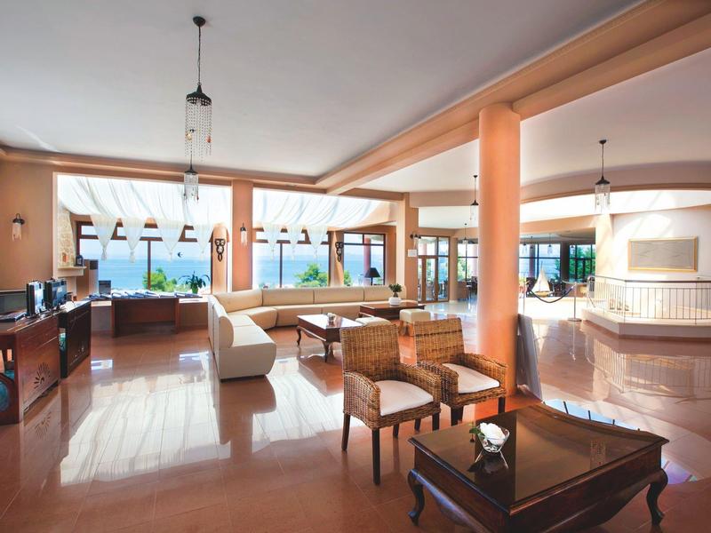 Großer, heller Wohnraum mit Stühlen, Sofas, Tisch und Panoramafenstern mit Meerblick.