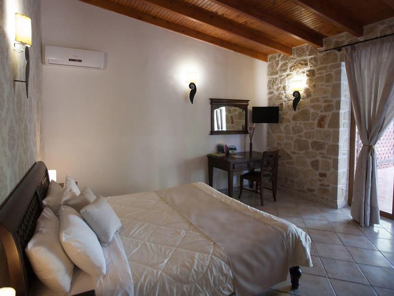 Helles Schlafzimmer mit Holzbalken, Steinwand, großem Bett, Schreibtisch und Glas-Tür zum Garten.