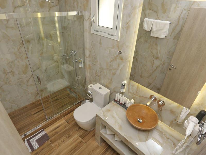 Kleines Bad mit braunem Waschbecken, Toilette, Glasdusche und Holzoptikboden.