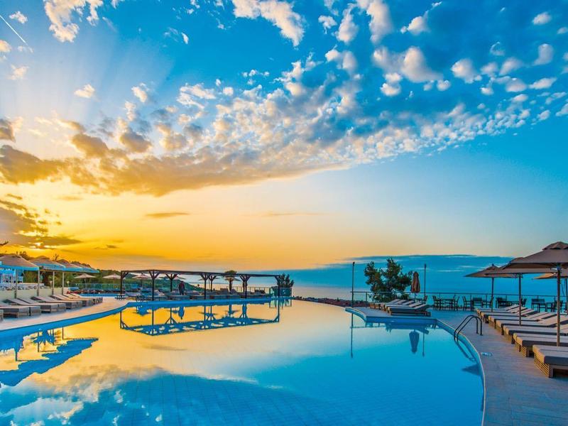 Sonnenuntergang über großem Pool mit Liegen und Schirmen, klarer Himmel mit Wolken.
