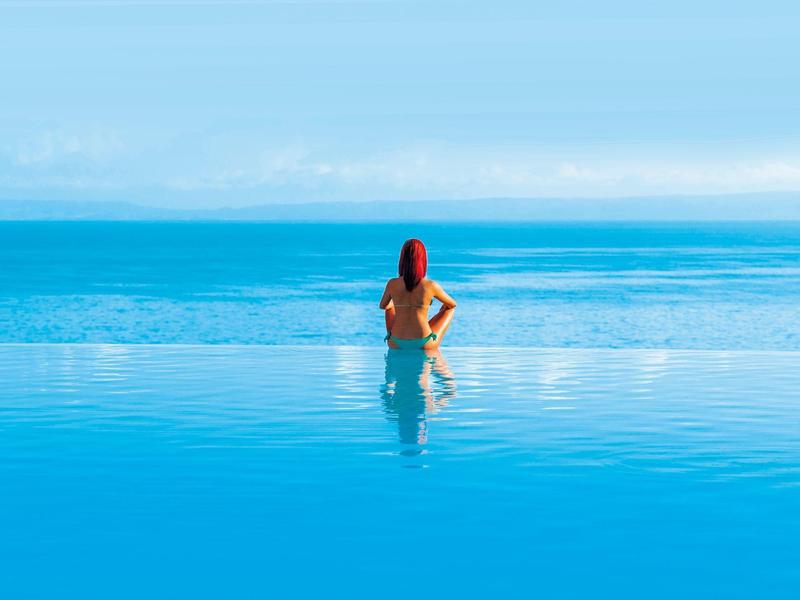 Frau mit roter Mütze steht hüfttief im ruhigen blauen Wasser unter klarem Himmel.