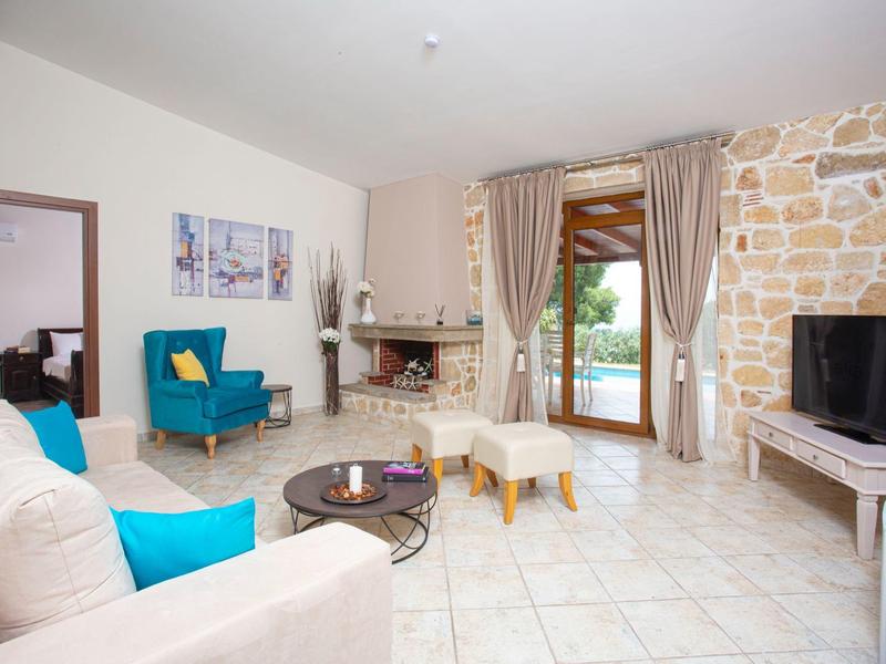 Helles Wohnzimmer mit Steinwand, Kamin, blauen Sesseln, Sofa und Fernseher auf hellen Fliesenboden.