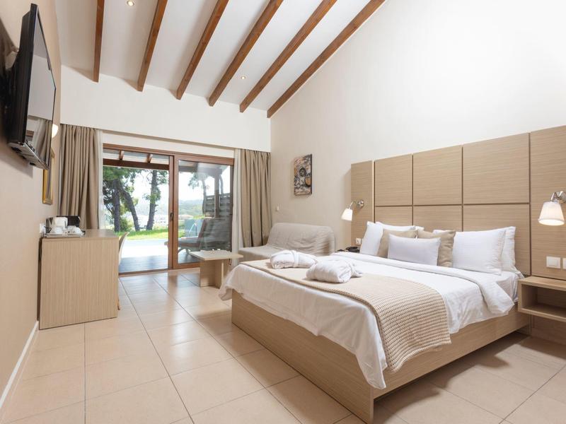 Helles Schlafzimmer mit Holzbalkendecke, großem Bett, Fernsehen und Terrasse mit Gartenausblick.