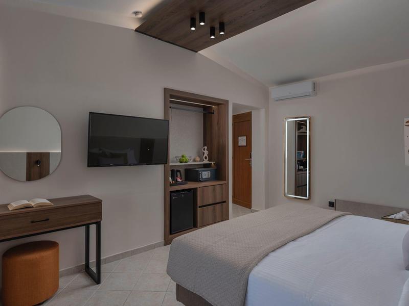 Modernes Hotelzimmer mit Doppelbett, Wandfernseher, Schreibtisch, Mini-Kühlschrank und Klimaanlage.