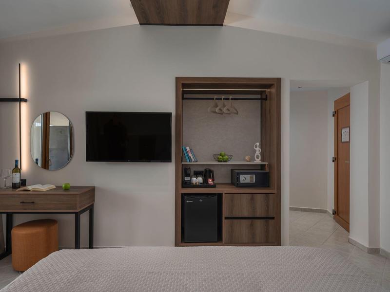 Moderner Hotelzimmer mit Bett, Wandfernseher, Schminktisch, Spiegel und offener Kleiderschrank.