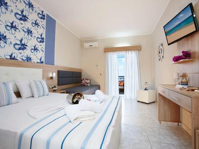 Helles Hotelzimmer mit großem Bett, blauer Wanddekoration, TV und Balkon mit Vorhang.